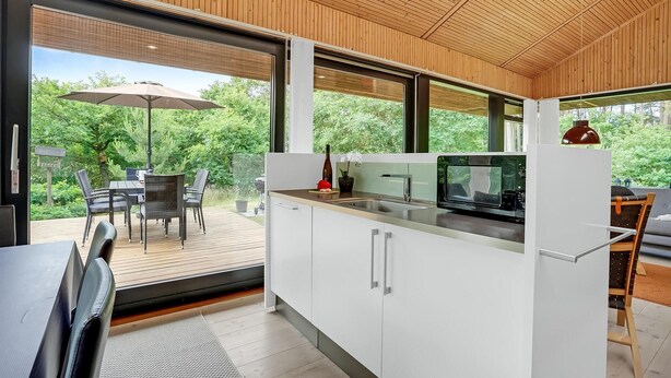 A modern kitchen with a large window, wooden ceiling, and a dining area with outdoor seating. - Nice home in Ebeltoft with WiFi (Ebeltoft)