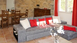 Un salon avec un canapé gris, des coussins rouges et blancs, une table à manger en bois avec des chaises, un meuble et une fenêtre avec des rideaux rouges.