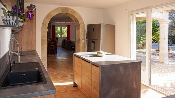 Une cuisine moderne avec une arche en pierre, un grand îlot central et une vue sur un jardin grâce à des portes vitrées.