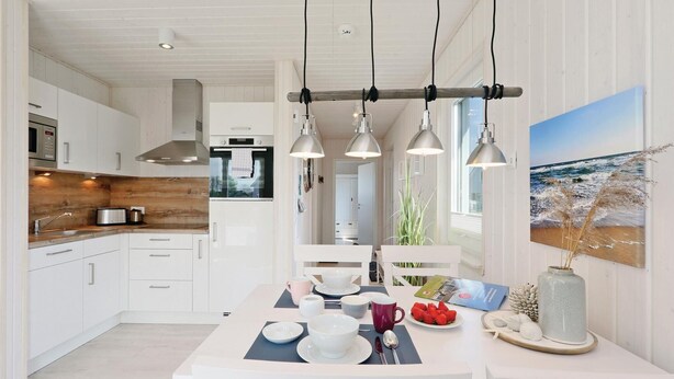 A modern kitchen with white cabinetry, a wooden countertop, and a central island with diningware. There are pendant lights above the island and a large window with a view of the ocean. - Stunning home in OstseeResort Olpenitz with sauna (OstseeResort Olpenitz)