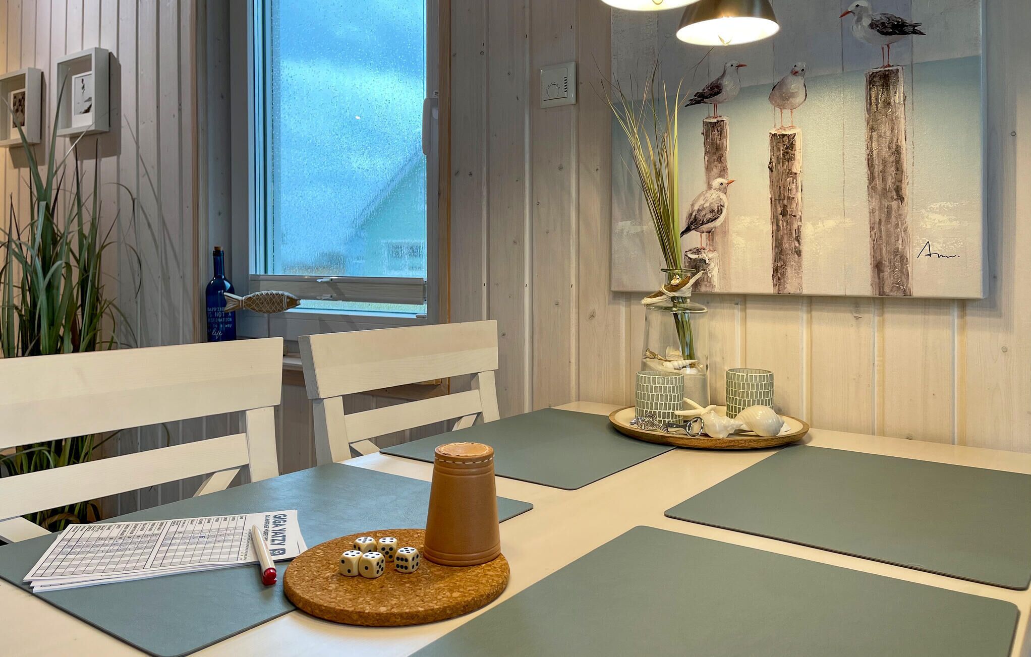 Un coin repas avec des chaises et des tables en bois, une fenêtre donnant sur un beau paysage et un tableau représentant des oiseaux accroché au mur.