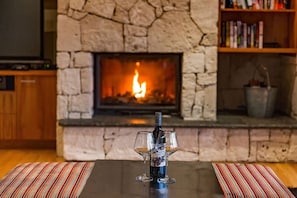 A fireplace with a fire, a bottle, and two glasses on a table.