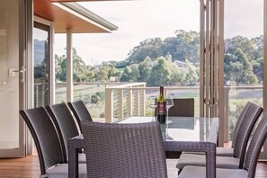 A balcony with a glass table, wicker chairs, and a bottle of wine.