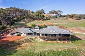 A modern two-story house with a large deck, surrounded by a natural landscape.