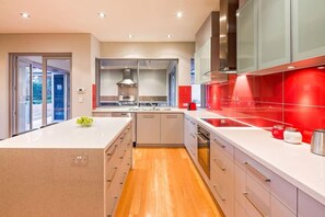 A modern kitchen with a central island, a built-in oven, and a red backsplash.