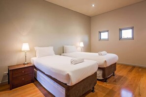 A hotel room with two beds, a wooden nightstand with a lamp, and two windows.