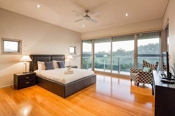 A modern bedroom with a large bed, a desk, and a view of the outdoors.