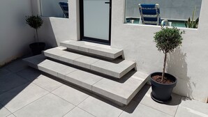 Un espace extérieur moderne doté d’une porte vitrée, d’un escalier menant à un balcon et de plantes en pot.
