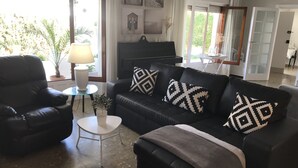 Un salon avec un canapé noir, une petite table ronde, une lampe et un piano.