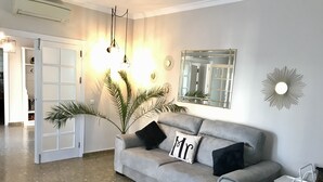 Un canapé gris avec deux coussins noirs et un coussin blanc, un miroir et un élément décoratif mural en forme de soleil, dans une pièce moderne au sol carrelé.