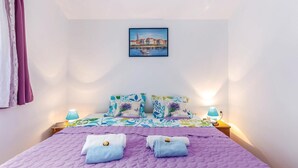 A neatly made bed with a purple quilt, two towels, and floral-patterned pillows. - Cozy apartment in Bakarac with house sea view (Bakarac)