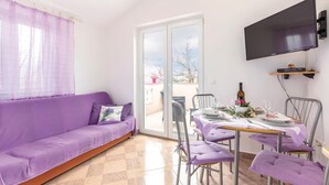 A room with a purple sofa, a dining table set for four, and a TV mounted on the wall. - Cozy apartment in Bakarac with house sea view (Bakarac)