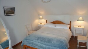 Et soveværelse med en stor seng, to sengeborde med lamper, en træsengeryg og et billede i ramme på væggen.