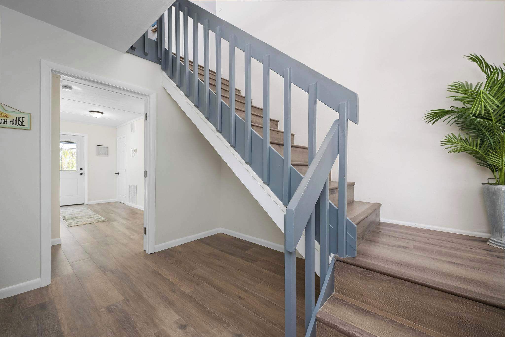 Eine Treppe mit blauer Handlauf, der zu einer Zwischenebene führt, einem Blumentopf und einem Holzboden.