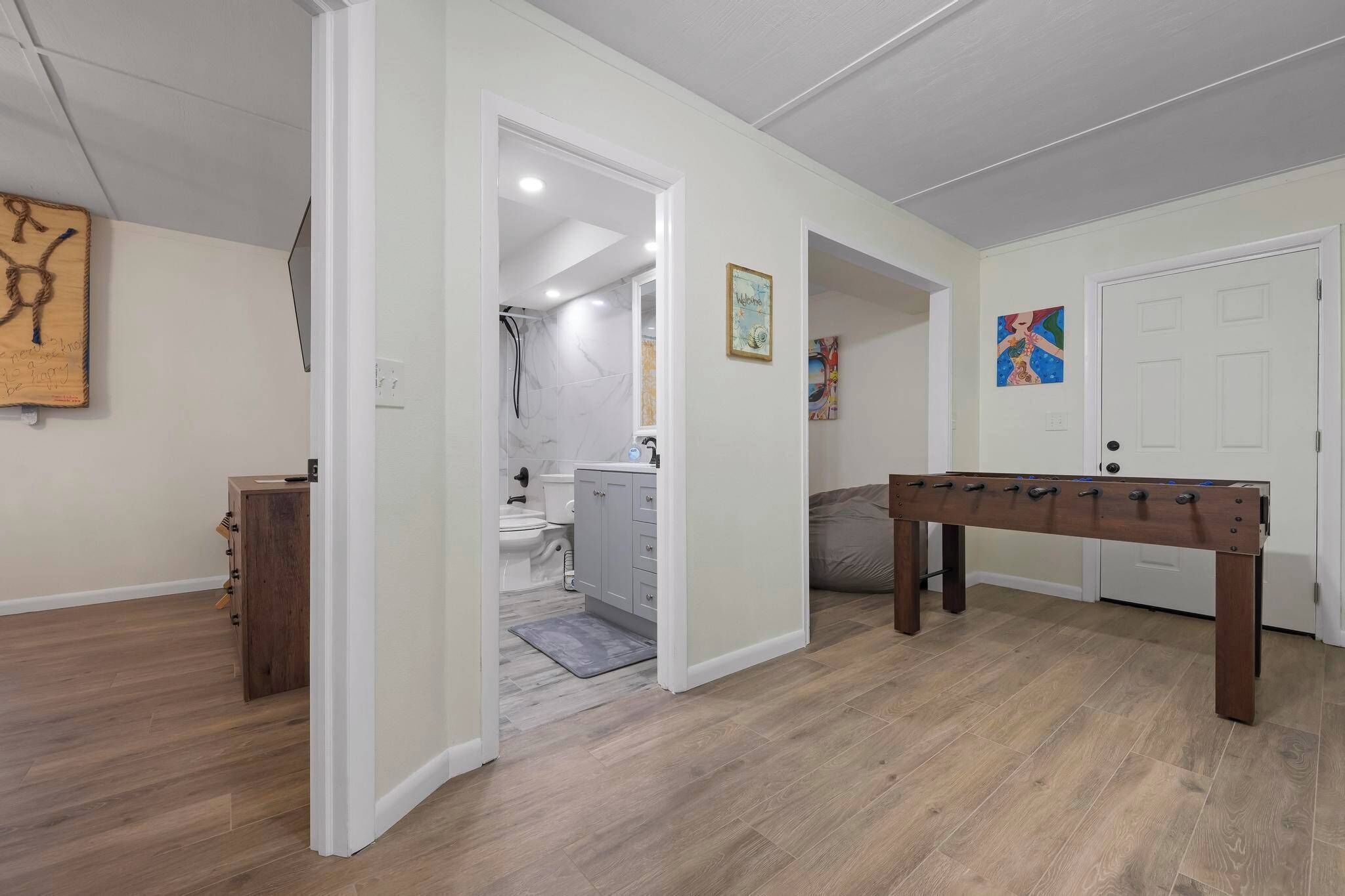 Une pièce avec un plancher en bois, une table de baby-foot et une porte donnant sur une salle de bain.