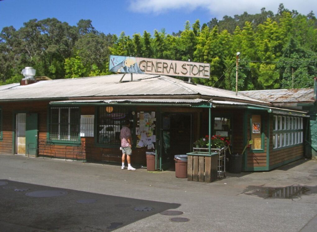 A general store with a signboard, wooden exterior, and a person standing outside.