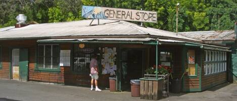 A general store with a signboard, wooden exterior, and a person standing outside.