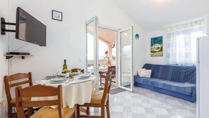 Un comedor con una mesa dispuesta para dos personas, un televisor montado en la pared y un sofá azul al fondo.