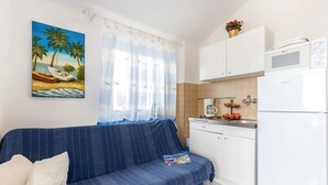 Un espacio habitable compacto con un sofá, una cocina que incluye microondas y un cuadro con una playa.