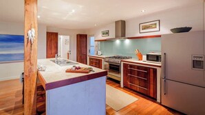 A modern kitchen with a central island, wooden cabinets, a stove, and a refrigerator. - Grace—Stunning Oceanview Escape on Cowaramup Bay (Gracetown)
