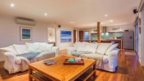 A living room with two white sofas, a wooden coffee table, and a kitchen in the background. - Grace—Stunning Oceanview Escape on Cowaramup Bay (Gracetown)