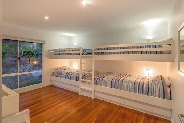 A room with three bunk beds, wooden flooring, and a large window.