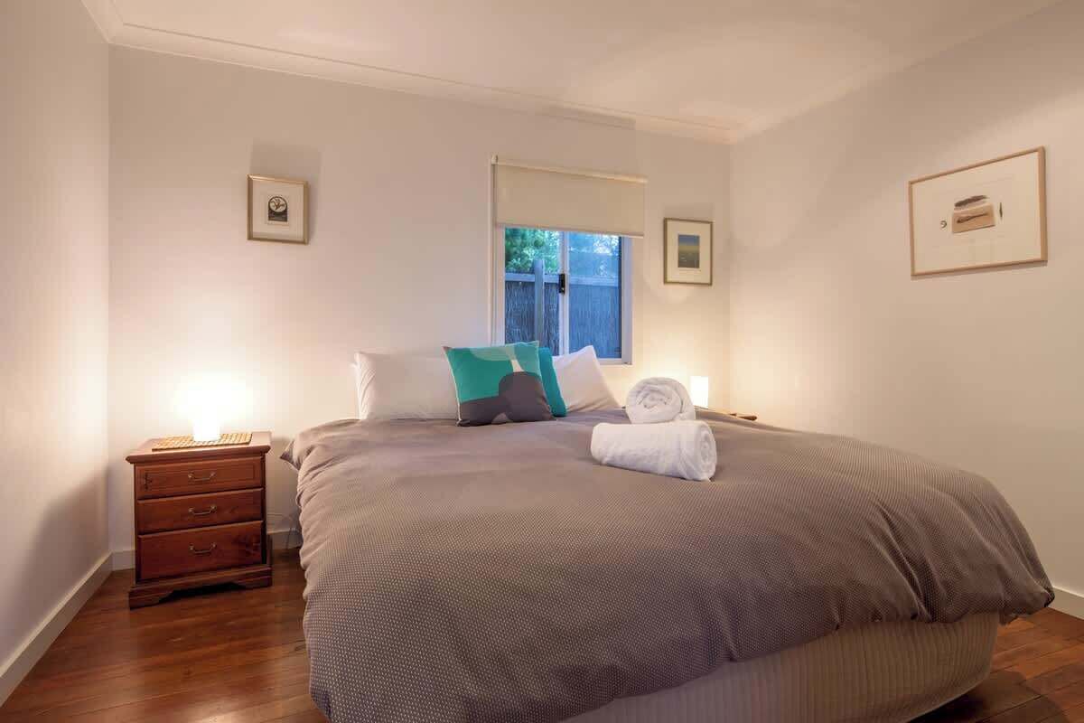 A bedroom with a large bed, a nightstand, a window, and framed pictures on the walls.