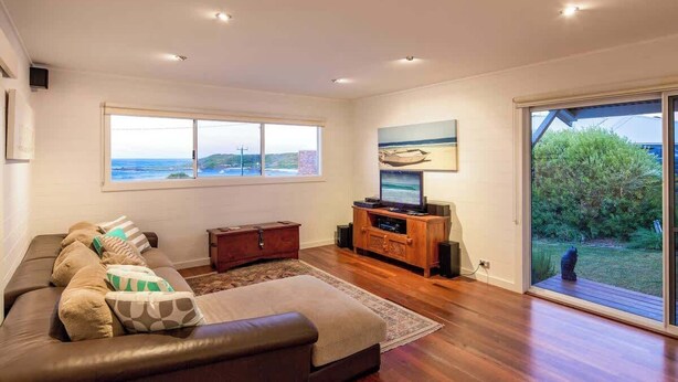 A modern living room with a leather sofa, a flat-screen TV, and a large window overlooking a scenic view. - Grace—Stunning Oceanview Escape on Cowaramup Bay (Gracetown)