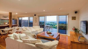 A spacious living area with a large sofa, a dining table, and a television. - Grace—Stunning Oceanview Escape on Cowaramup Bay (Gracetown)