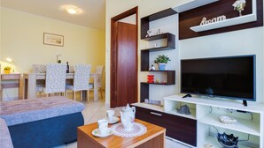 A living room with a TV, shelves with decorative items, a dining area with chairs and a table, and a sofa. - 2 bedroom amazing apartment in Porec (Porec)