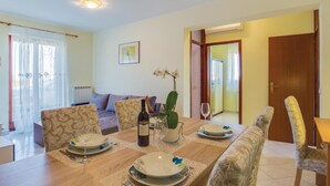 A dining area with a wooden table set for two, a sofa, and a potted orchid. - 2 bedroom amazing apartment in Porec (Porec)