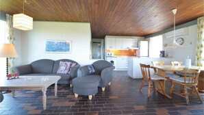 A cozy living area with a sofa, ottoman, and dining table with chairs. A kitchen is visible in the background with a microwave and sink. - 3 bedroom amazing home in Frøstrup (Frøstrup)