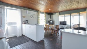 A kitchen with white cabinets, a wooden ceiling, a dining area with chairs, a TV, and a clock on the wall. - 3 bedroom amazing home in Frøstrup (Frøstrup)