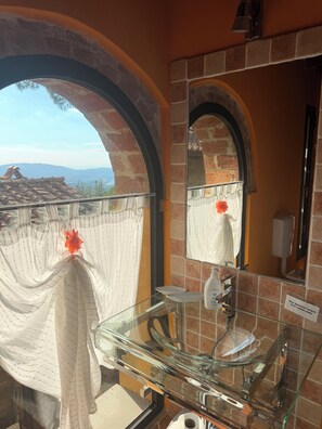 A bathroom with a glass sink, a mirror, and a view of the outdoors through an arched window. - the Casellina (Casa Biondo)