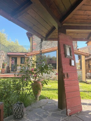 A stone building with a wooden porch, a potted plant, and a metal railing.