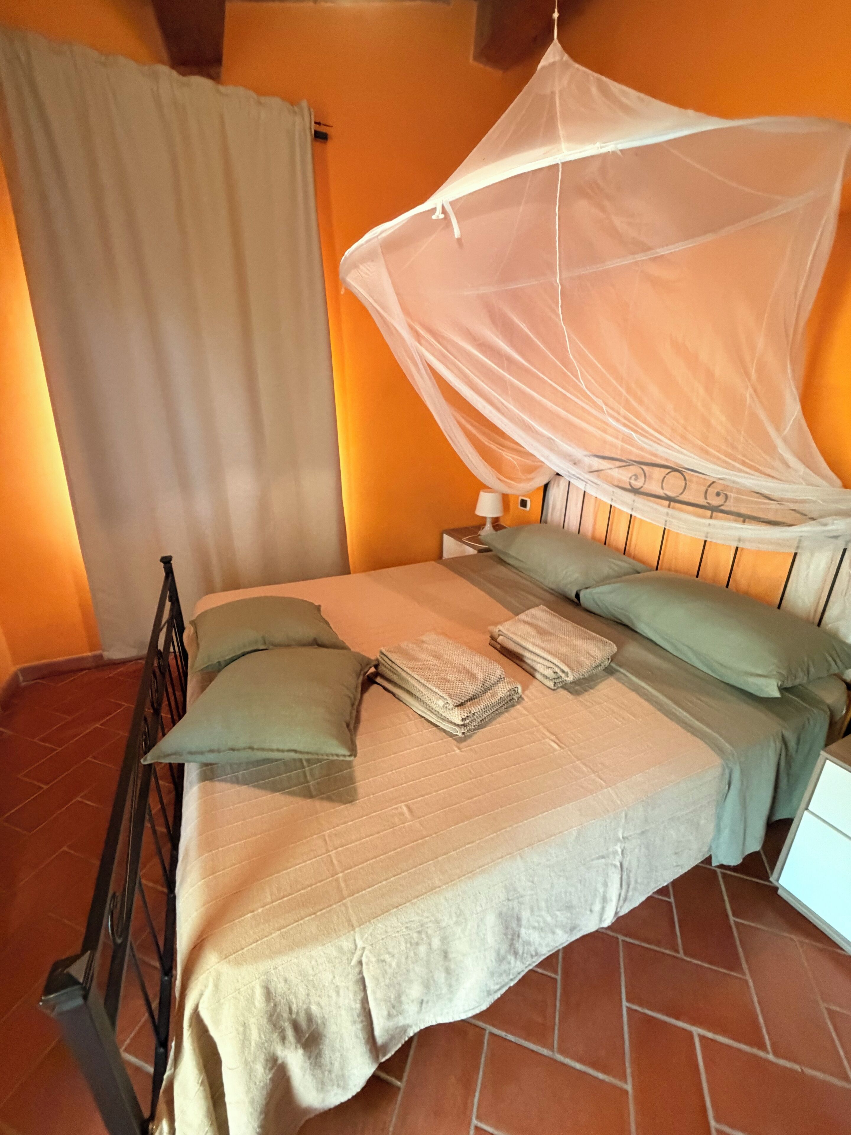 Una camera da letto con un letto, una zanzariera, un comodino e una finestra con tende.
