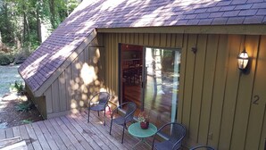 A wooden cabin with a sloped roof, a porch with metal chairs and a small table, and a sliding glass door leading to an interior with a dining table and chairs. - Seven Springs Cabin - Bear Claw Chalet - Authentic, Pet Friendly Log Cabin (Champion)