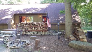 A rustic lodge with a stone fire pit, a stack of firewood, and an American flag. - Seven Springs Cabin - Bear Claw Chalet - Authentic, Pet Friendly Log Cabin (Champion)