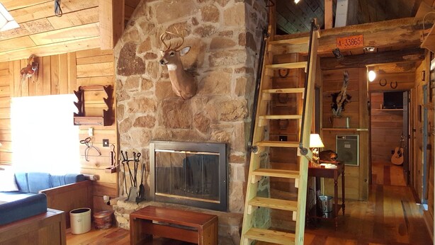 A rustic interior with a stone fireplace, wooden furniture, and a ladder leading to a loft. - Seven Springs Cabin - Bear Claw Chalet - Authentic, Pet Friendly Log Cabin (Champion)