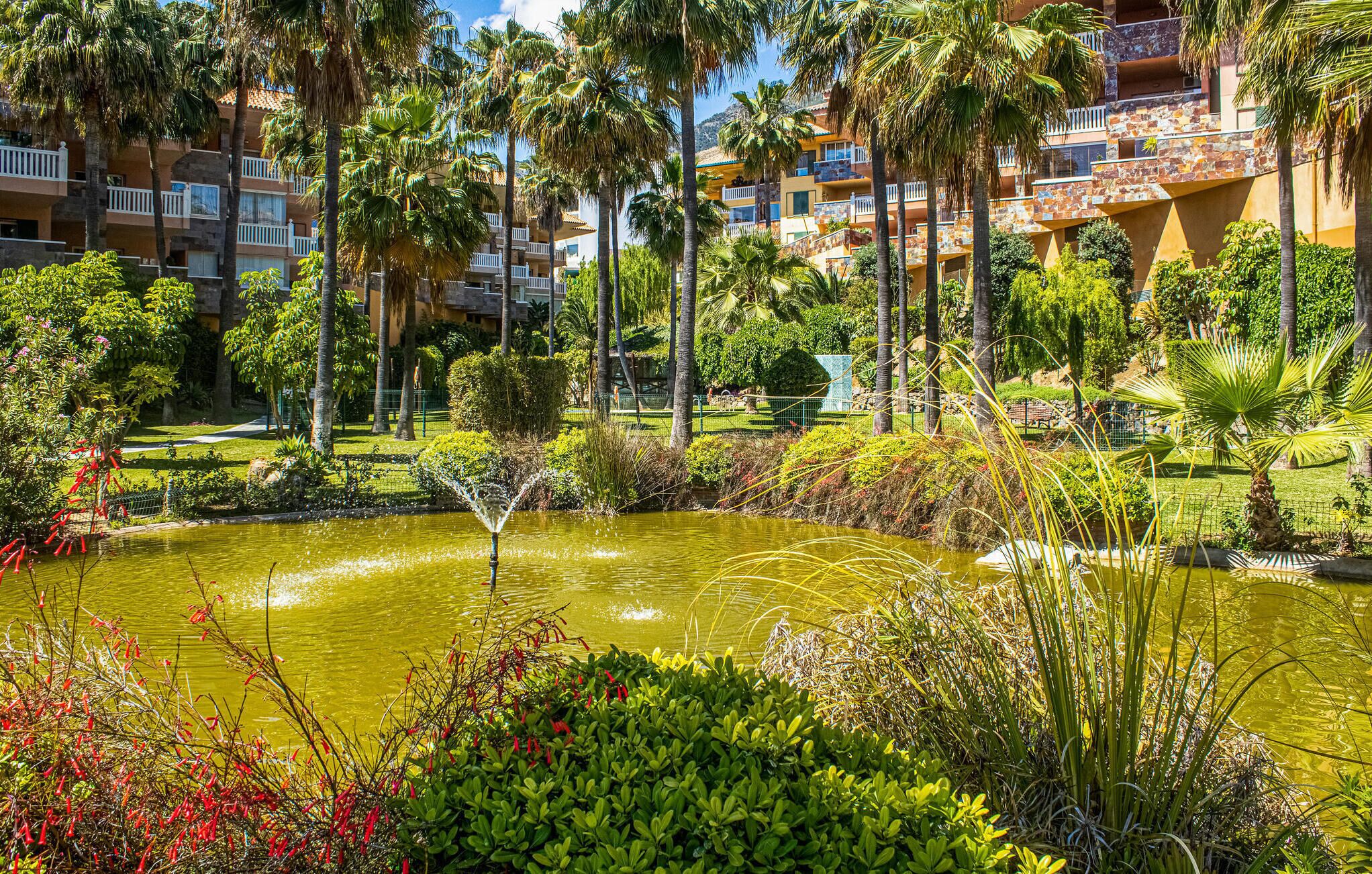 A hotel with multiple balconies, lush greenery, and a central water feature.