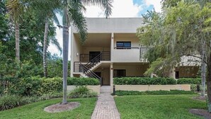 A building with a central staircase leading to an upper level, surrounded by well-maintained greenery and a paved walkway. - Whole Home Villa in Hyde Park at Pelican Bay community with private pool/beach! (Naples)