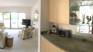 A spacious living room with a glass coffee table, a sofa, and a television. There is a kitchen area with a microwave and a refrigerator. - Whole Home Villa in Hyde Park at Pelican Bay community with private pool/beach! (Naples)