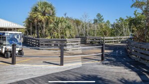 A wooden boardwalk with a vehicle parked on the left, surrounded by trees and a building with a sign that reads "Marker 3". - Whole Home Villa in Hyde Park at Pelican Bay community with private pool/beach! (Naples)