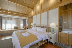 Ein Schlafzimmer mit Holzwänden, einem großen Bett, Nachttischlampen, einem kleinen Tisch und einer Badewanne.
