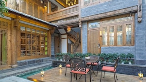 A traditional wooden building with a wooden staircase, a small outdoor seating area with chairs and a table, and a small water feature. - Floral Hotel Lijiang Huazizai (Lijiang)