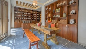 A kitchen with wooden cabinets, a large wooden table, and shelves filled with dishes and kitchenware. - Floral Hotel Lijiang Huazizai (Lijiang)