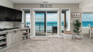 Ein Wohnzimmer mit Fernseher, Unterhaltungseinheit und großem Fenster mit Blick auf einen Strand.