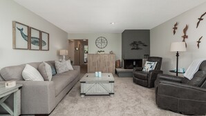 Ein Wohnzimmer mit Sofa, Sessel, Couchtisch, Kamin und Wandbildern.