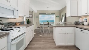 Eine moderne Küche mit weißen Schränken, einem eingebauten Backofen und einer Mikrowelle. Es gibt einen Essbereich mit Blick auf den Ozean.