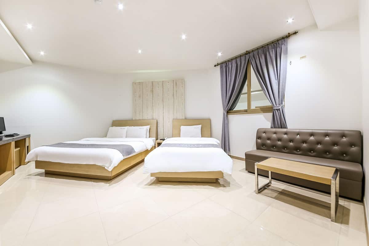 Una habitación de hotel con dos camas, un sofá, una mesita y un televisor.